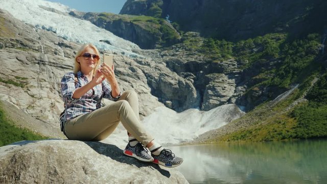 A woman tourist does selfie on the background of a glacier in Norway