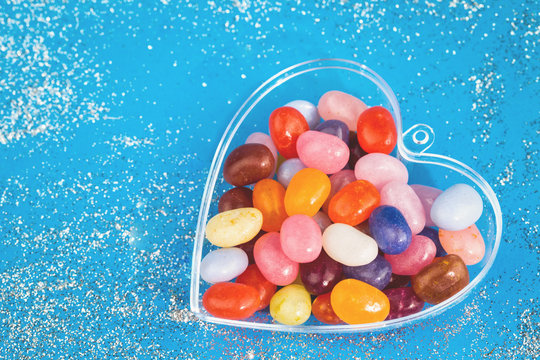 One Heart With Colorful Jelly Bean Candies On Blue Background With Copy Space Closeup Flat Lay. Love And St Valentines Day Concept