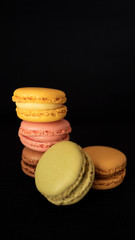 Assortment of traditional French macaroons or macarons, selection of different colors and flavors, very light bite-size confectionery, stacked high, with black background and selective focus