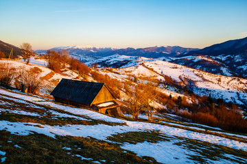 Lonely house standing on mountain slope. Melting snow in spring