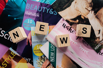 top view of pile of different tabloid magazines and wooden cubes with word news on surface - obrazy, fototapety, plakaty