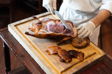The chef is cutting the duck skin from the Beijing duck with a very sharp knife at a famous Chinese restaurant.