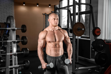 Fototapeta na wymiar Muscular man training with dumbbells in gym