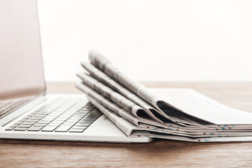 laptop and stack of newspapers on wooden tabletop