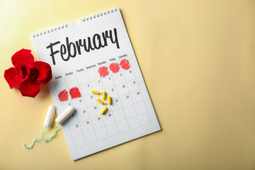 Menstrual calendar with tampons, pills and red flower on color background