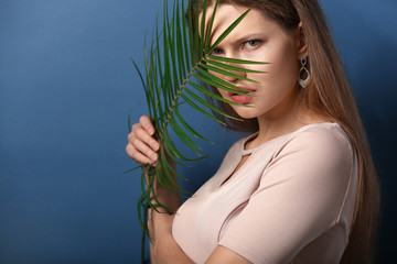 Fototapeta premium Portrait of beautiful woman with green tropical leaf on color background