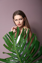 Portrait of beautiful woman with green tropical leaf on color background