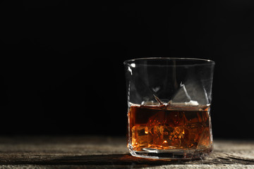 Glass of whiskey on wooden table against dark background