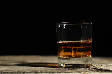 Glass of whiskey on wooden table against dark background