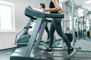 Fototapeta na wymiar Two young fitness healthy women on treadmill in the sport modern gym. Fitness, sport, training, people concept