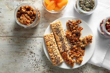 Plate with tasty baked granola and bars on wooden background