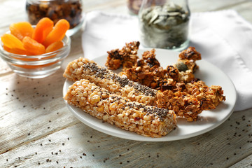 Plate with tasty baked granola and bars on wooden background