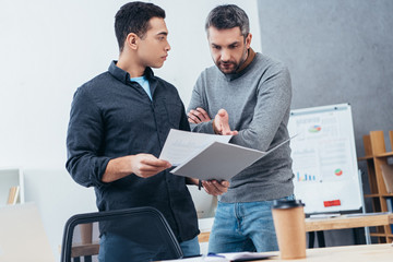 serious businessmen holding folder with papers and discussing project in office