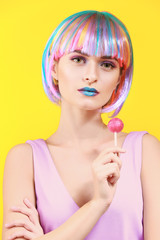 Beautiful young woman with unusual makeup and sweet lollipop on color background