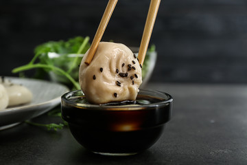 Dipping of tasty Chinese dumpling into bowl with sauce