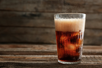 Glass of soda with ice on wooden table