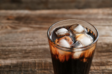 Glass of soda with ice on wooden table, closeup