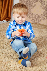 A little boy is sitting on the carpet and playing in the phone.