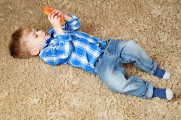 A little boy is lying on the carpet and playing in the phone. Little boy using smartphone.