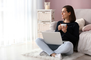 Young woman with laptop drinking coffee at home