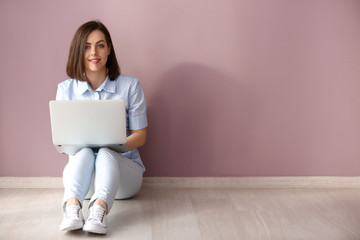 Young woman with laptop sitting near color wall