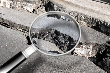 Cracked asphalt road damaged after a structural failure - Concept image seen through a magnifying glass