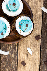 Blue ice cream with chocolate in coconut bowl on wooden background.