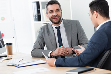 handsome smiling businessman looking at young man colleague working in office