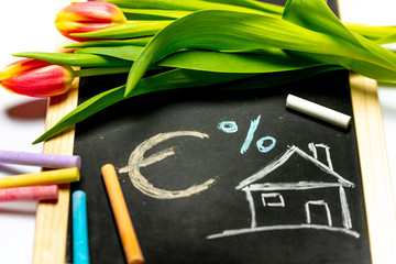 a house drawn with chalk on a blackboard with spring flowers in the background, with space for text