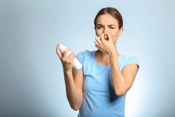 Beautiful young woman with deodorant feeling smell of sweat on light background. Concept of using...