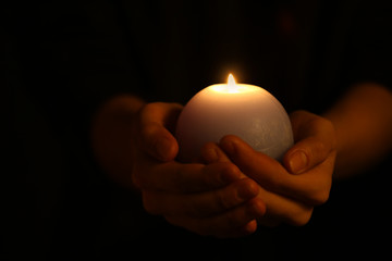 Female hands with burning candle in darkness