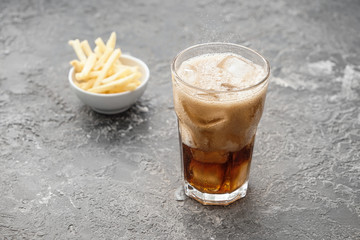 Glass of tasty cola drink with french fries on grunge table