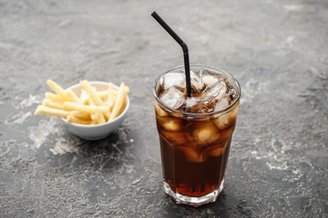 Glass of tasty cola drink with french fries on grunge table