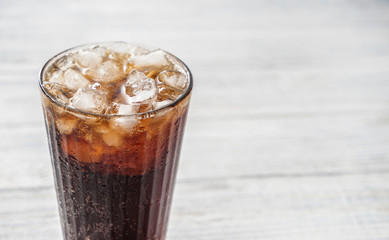 Glass of tasty cold cola drink on white wooden table