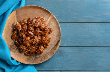 Plate with candied pecan nuts on wooden background - obrazy, fototapety, plakaty