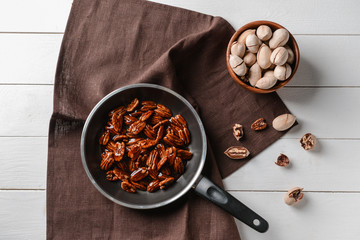 Frying pan with candied pecan nuts on white table