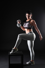 Sporty muscular woman with dumbbell on dark background