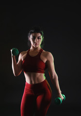 Sporty muscular woman with dumbbells on dark background