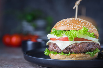 Hamburger with beef meat burger and fresh vegetables on dark background. Tasty fast food.