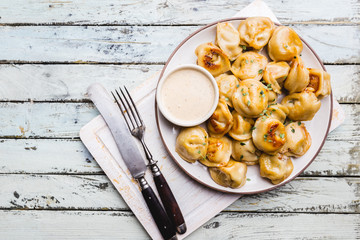 Delicious fried dumplings with sauce on a white plate over wooden background, top view
