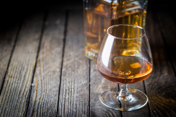 Glass and a bottle of brandy or cognac on the wooden table.