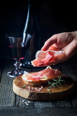 Female hand putting prosciutto on bread over dark wooden background. Sandwich cooking.
