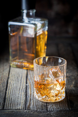 Glass and a bottle of whiskey with ice on dark wooden table