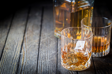 Glass and a bottle of whiskey with ice on dark wooden table