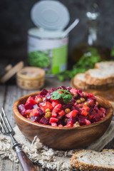 Russian beetroot salad vinaigrette in wooden bowl with rye bread, rustic background