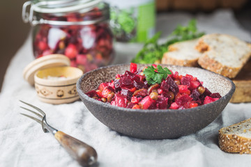 Russian beetroot salad vinaigrette in a bowl with rye bread, rustic background