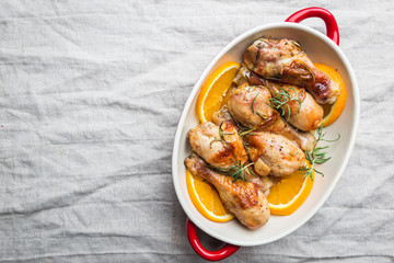 Baked chicken drumstick in a dish with orange and rosemary, top view