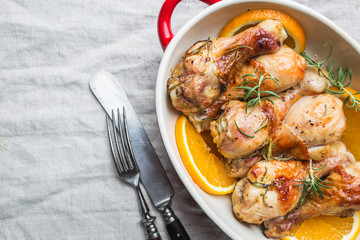 Baked chicken drumstick in a dish with orange and rosemary, top view