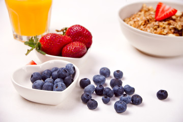 A plate with muesli, bowls with berries on the white table