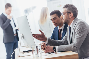 serious professional businessmen using desktop computer and discussing work in office